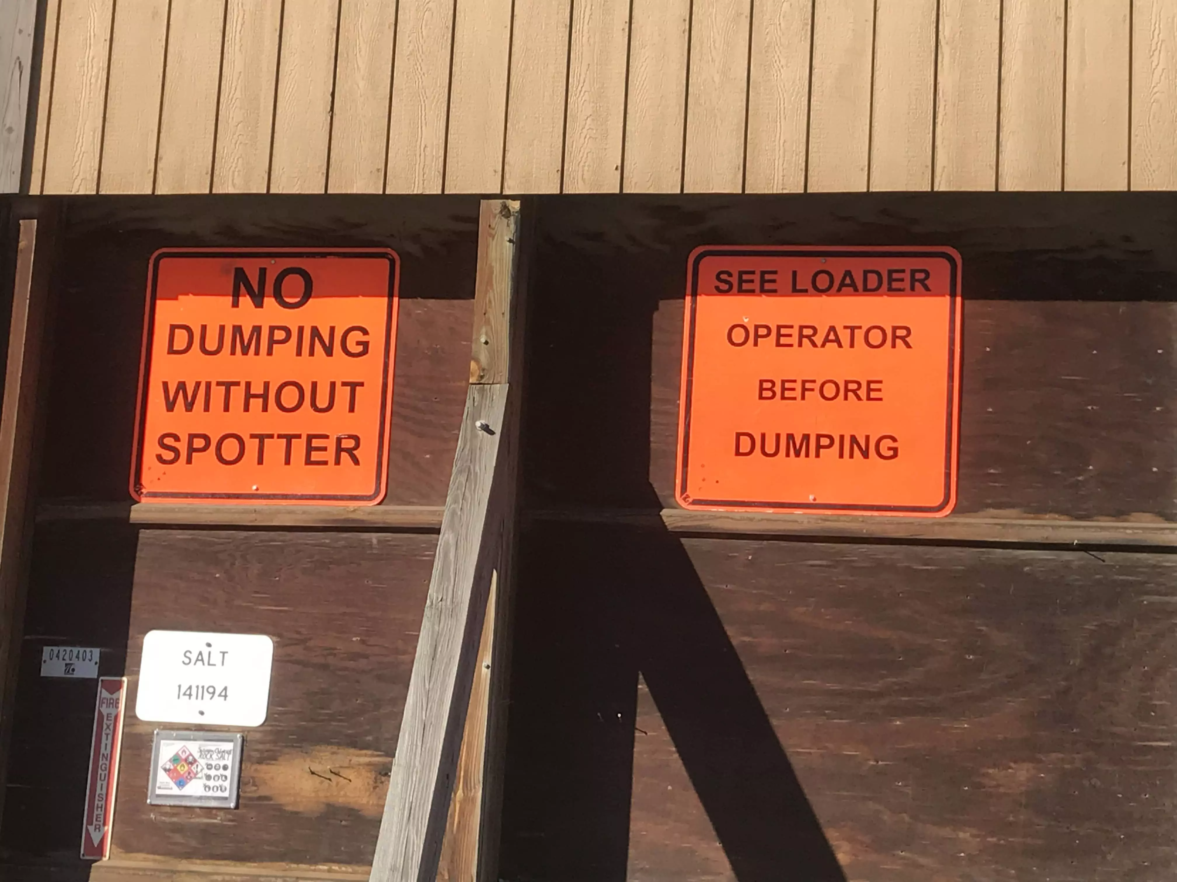 A PennDOT stockpile wall displays signs, including 'No dumping without spotter' and 'See loader operator before dumping.'